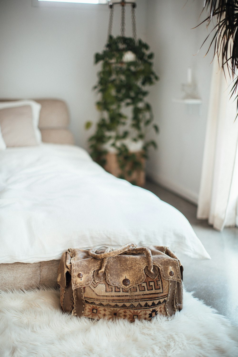 a white bed with a fur rug and a bag on the floor