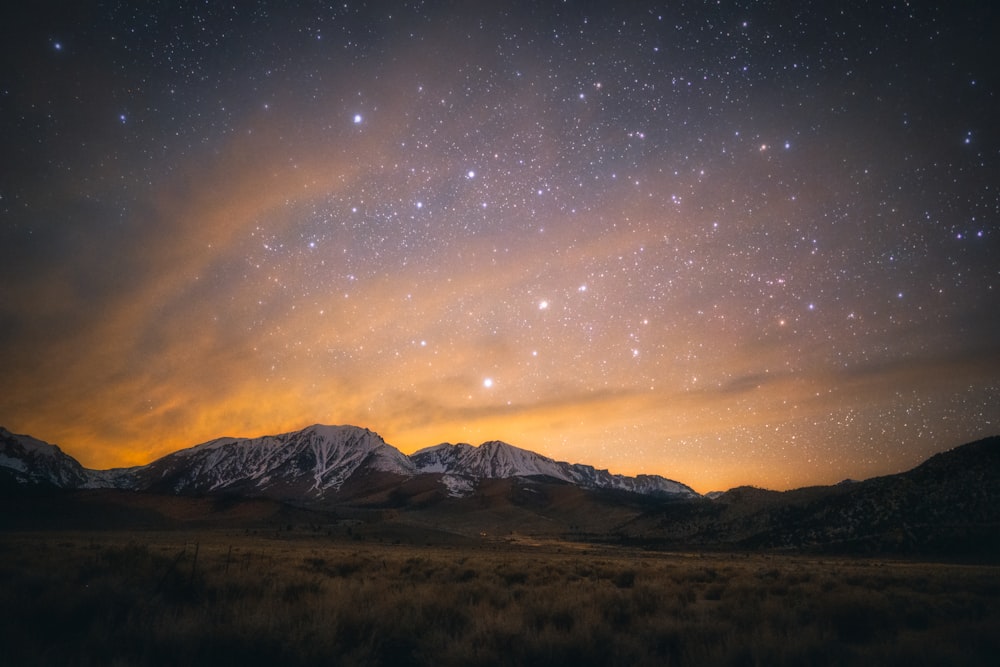 brown grass field near mountain under blue sky during night time