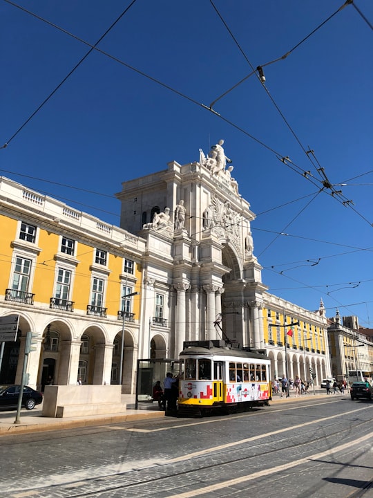 yellow and white tram on road near beige concrete building during daytime in Praça do Comércio Portugal