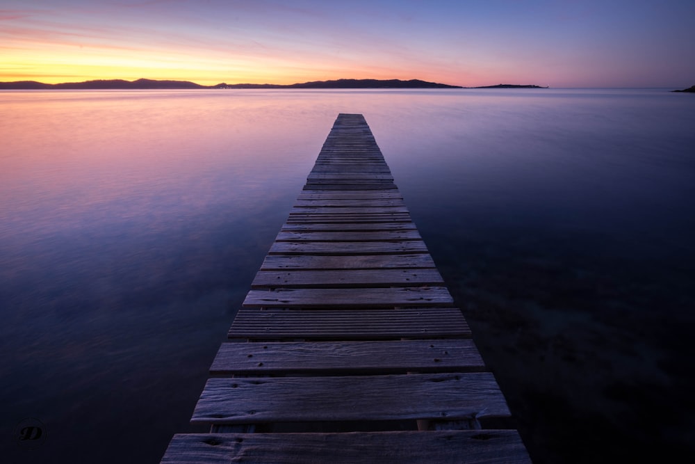 brown wooden dock on body of water during sunset