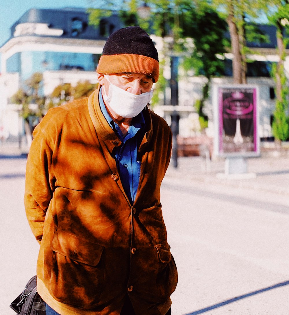 man in brown coat and white taqiyah cap standing on street during daytime