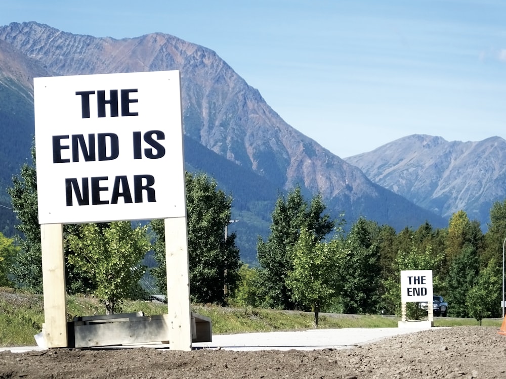 white and black wooden signage near green trees and mountain during daytime