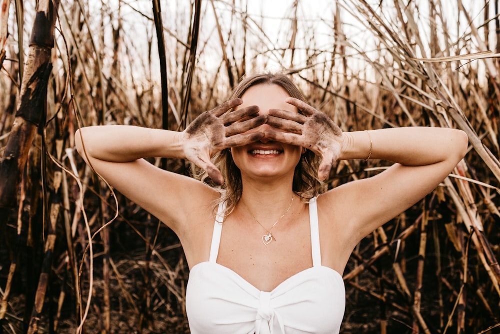 woman in white spaghetti strap top standing near brown grass during daytime