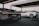 Two luxury sports cars are showcased in a modern, open garage. The foreground features a sleek black car with intricate tail light and exhaust details, while a white sports car stands in the background. The setting suggests a high-end automotive event or display.