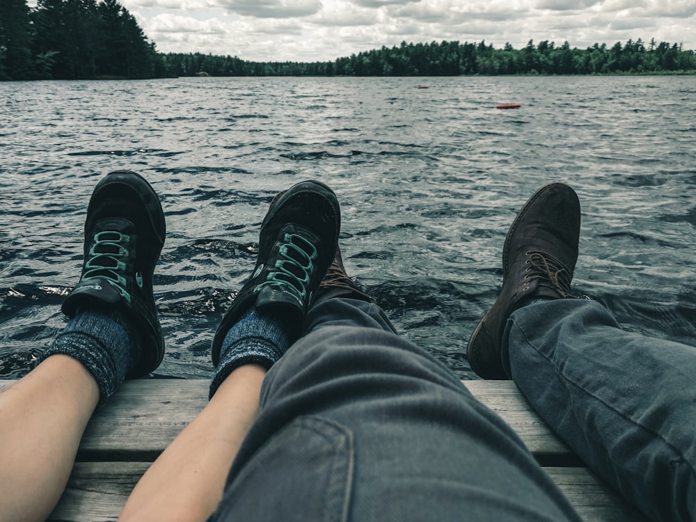 persona in jeans blu denim e scarpe nere seduta sul molo di legno marrone sopra il corpo di vicino vicino vicino vicino vicino