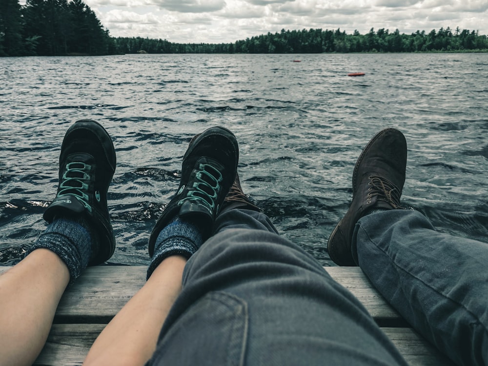 person in blue denim jeans and black shoes sitting on brown wooden dock over body of near near near near