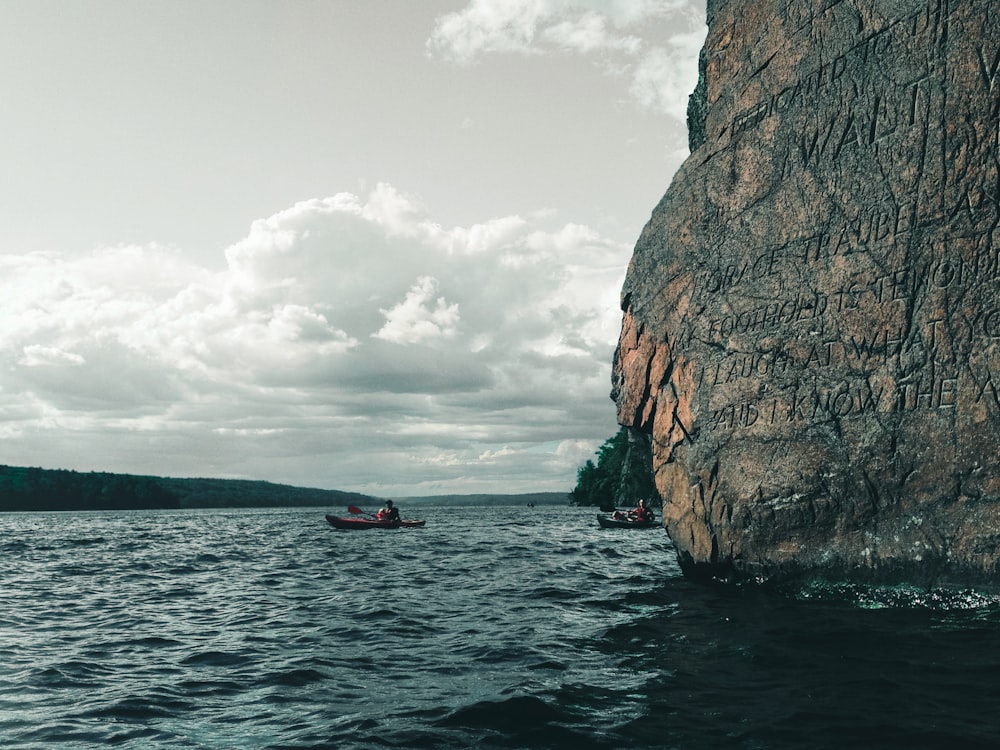 red boat on sea near brown rock formation under white clouds during daytime