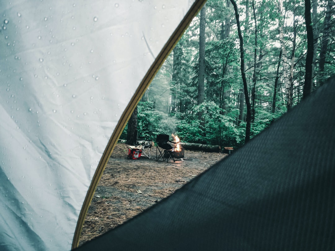 man in black shirt sitting on brown wooden bench, Rainy day in camp but had a nice fire going