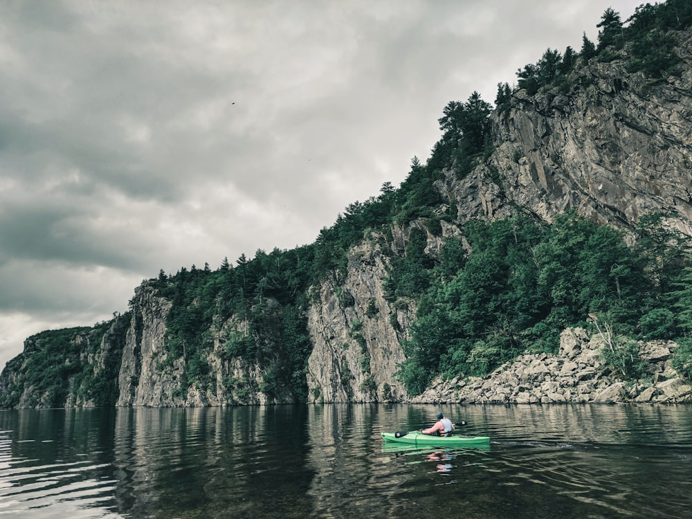 person riding on red kayak on river near mountain during daytime