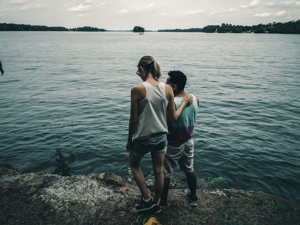 woman in white tank top and gray shorts standing on rocky shore during daytime