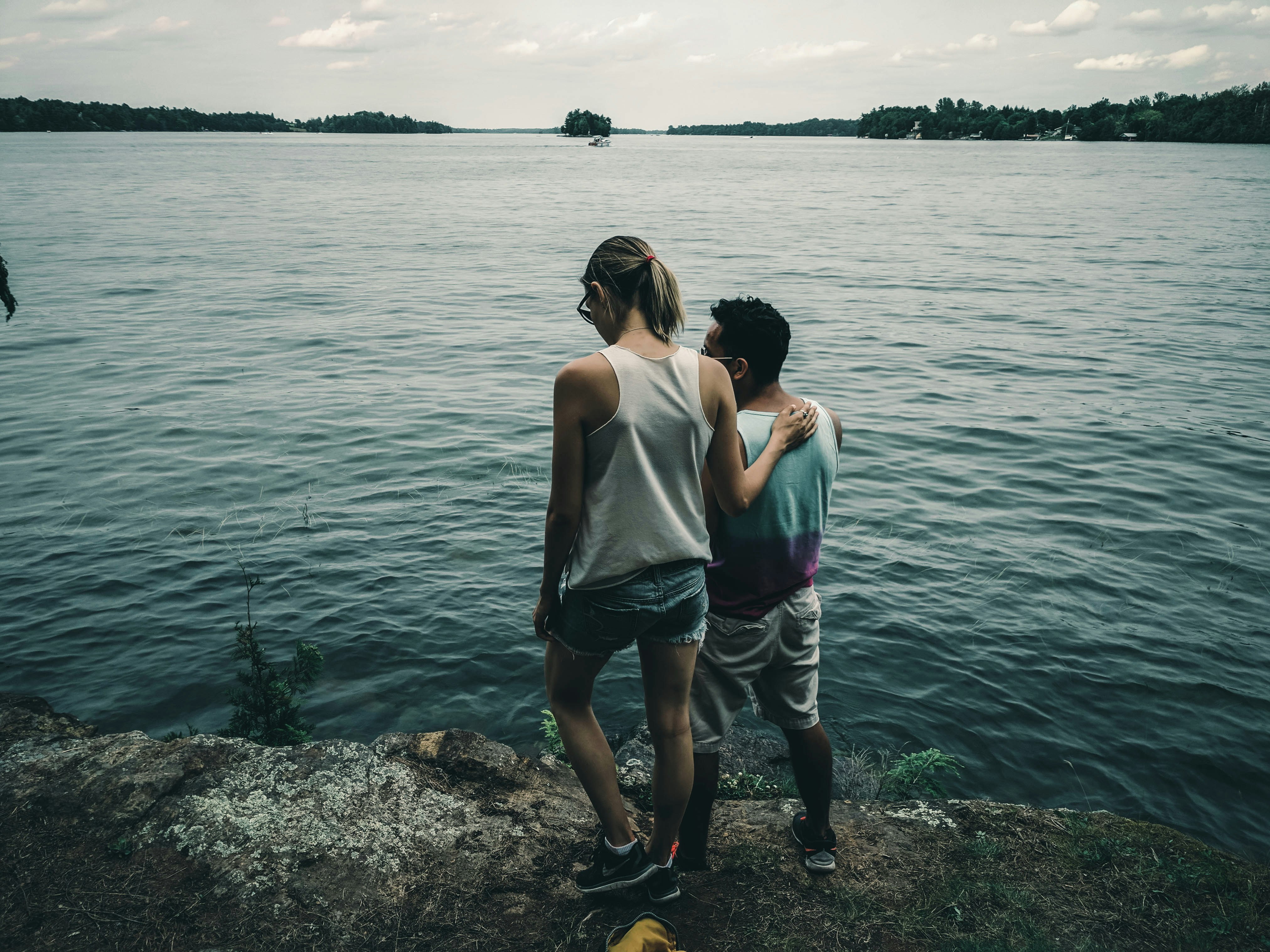 woman in white tank top and gray shorts standing on rocky shore during daytime