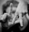 A close-up of two hands, with fingers forming the word 'LOVE' in sign language. The hands are adorned with rings, including a heart-shaped one. The image is in black and white.