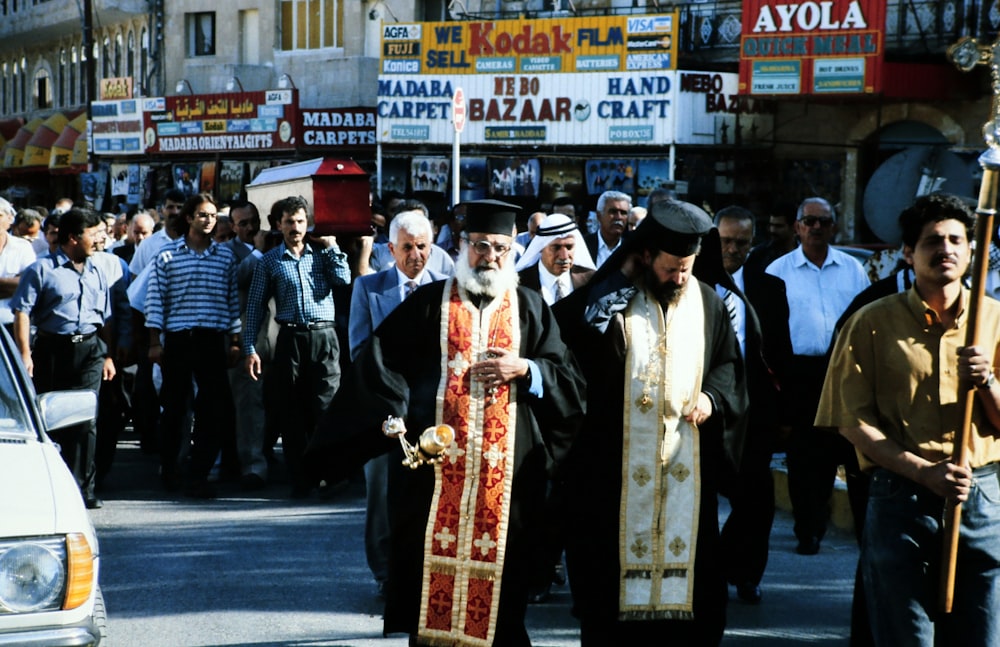 Persone in abito tradizionale bianco e nero in piedi sulla strada asfaltata grigia durante il giorno