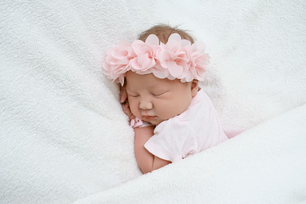 baby in white shirt lying on white textile