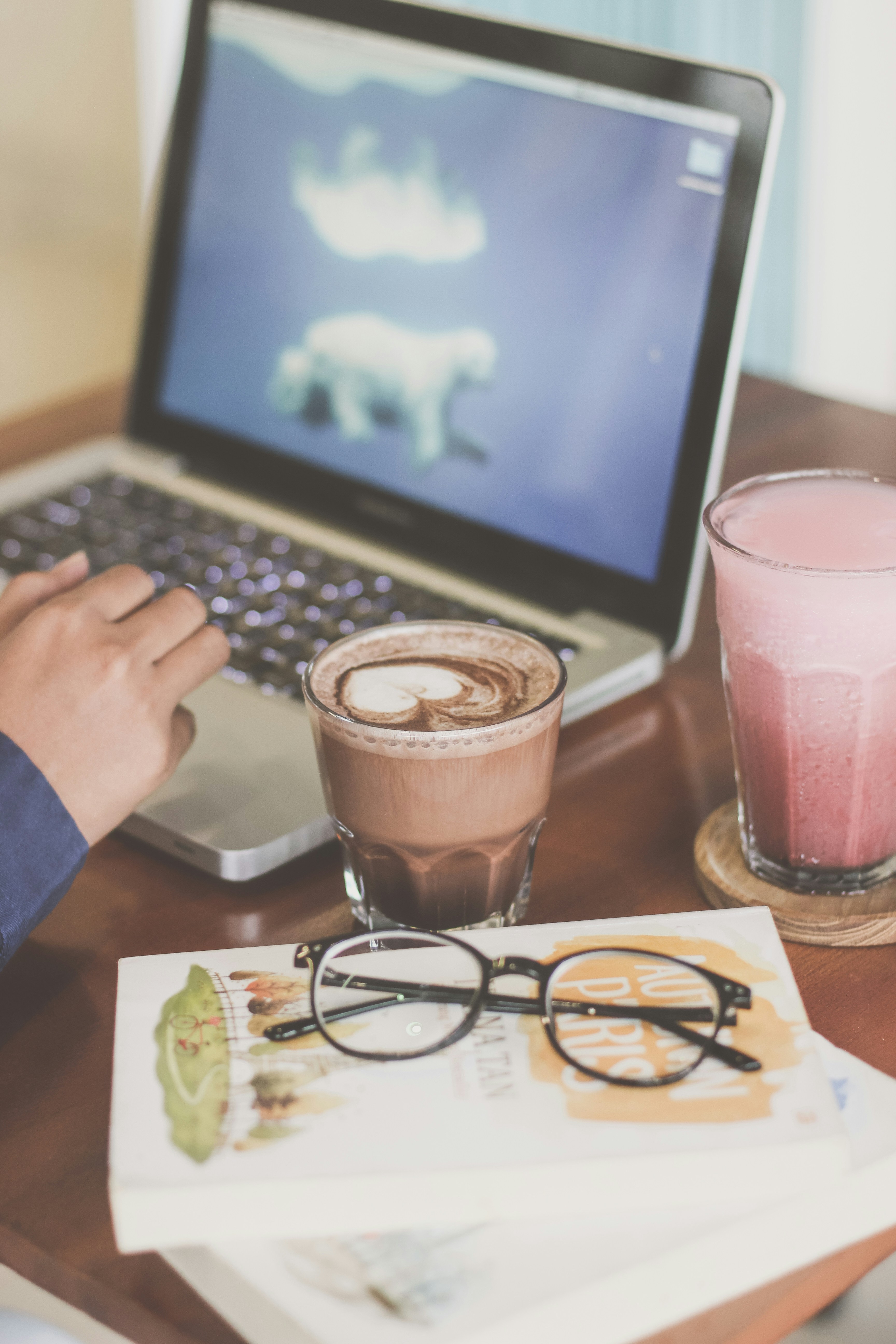 Orang yang memegang gelas minum bening di samping MacBook Pro