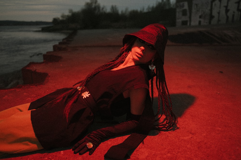 검은 긴 소매 셔츠와 붉은 히잡을 쓴 여자가 낮에 갈색 모래 위에 앉아 있다