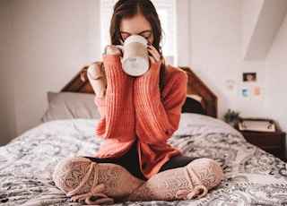 woman in red knit sweater holding white ceramic mug