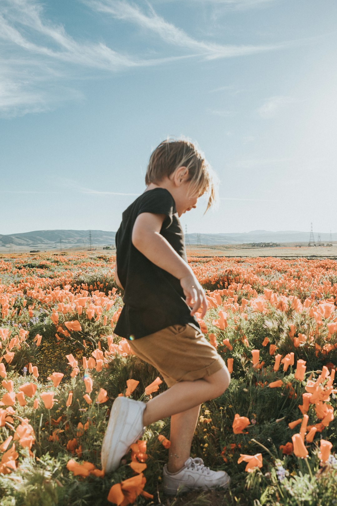 woman in black t-shirt and brown skirt standing on flower field during daytime