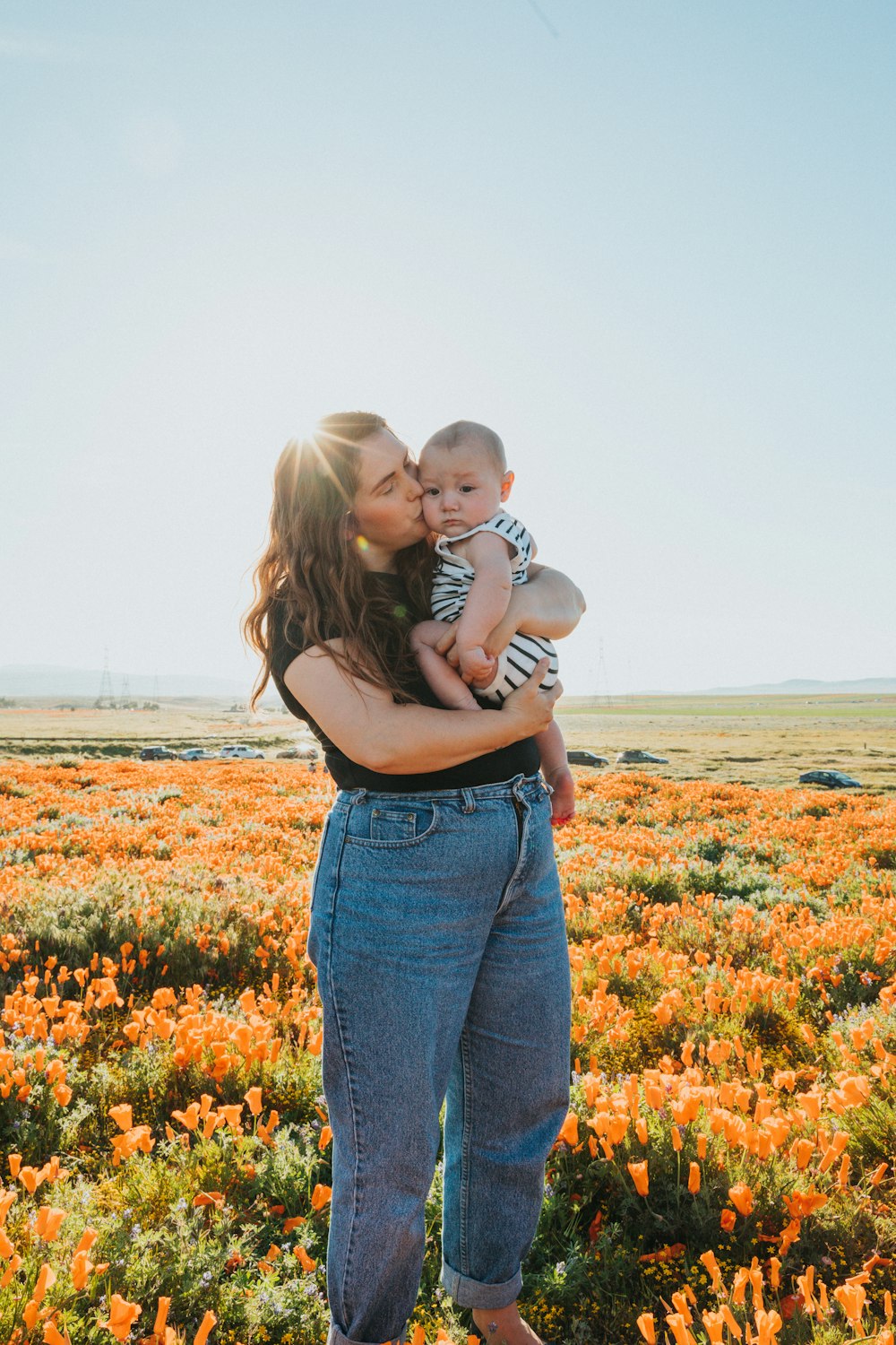 woman in black tank top and blue denim jeans carrying baby in white shirt on flower