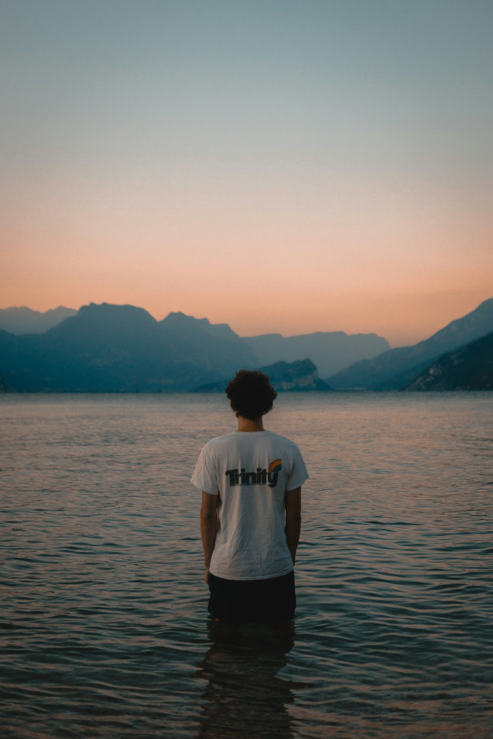 man in white t-shirt standing on sea shore during daytime