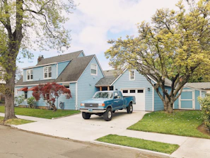 A cozy house exterior with a small garden and a car parked in the driveway under a clear blue sky.