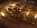 A large stack of shiny gold bars neatly arranged on a reflective surface, creating an impression of wealth and opulence. The bars are aligned in rows, with light glinting off their polished surfaces.