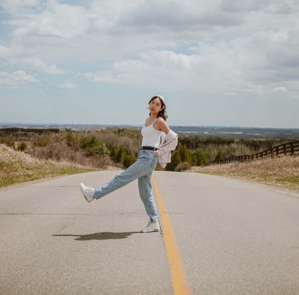 woman in white long sleeve shirt and blue denim jeans standing on gray asphalt road during