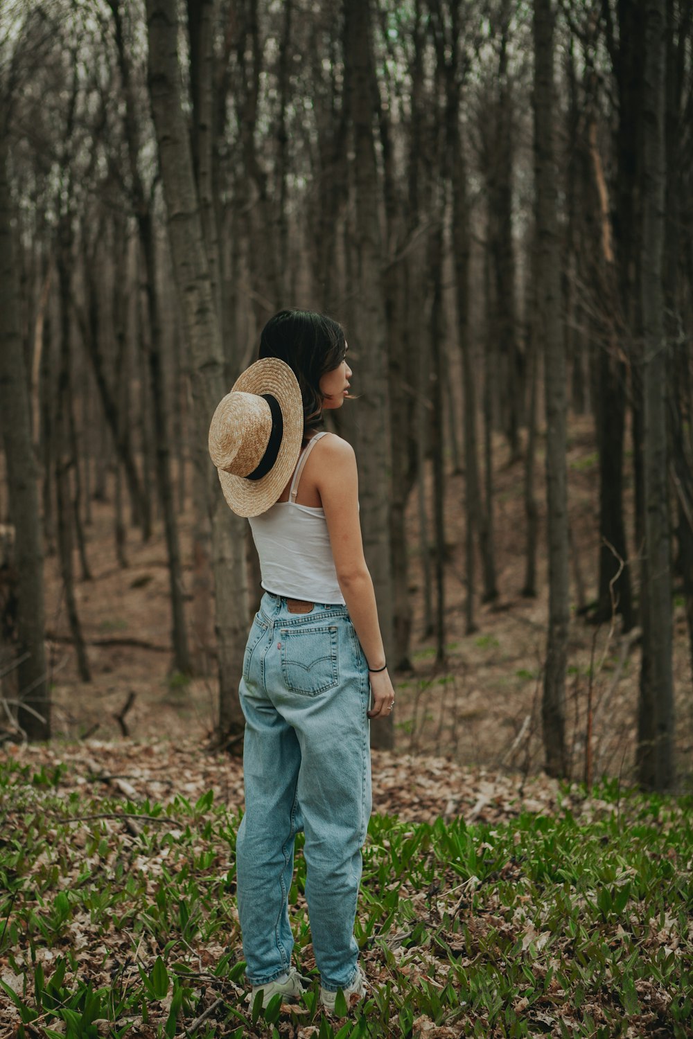 woman in white tank top and blue denim jeans wearing brown straw hat standing on green