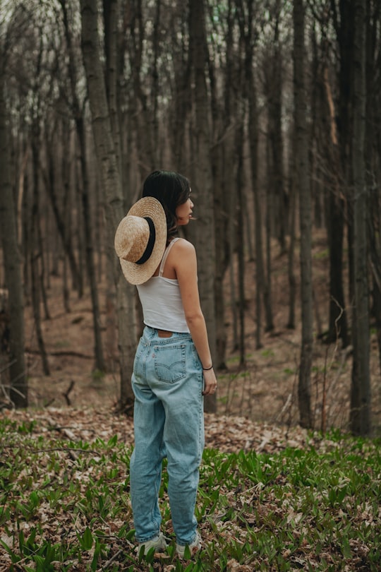 woman in white tank top and blue denim jeans wearing brown straw hat standing on green in Caledon Canada