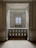 An elegant space with marble walls and a decorative balustrade. A window with a grid design is centered in the background, allowing soft light to enter the room, creating a calm and serene atmosphere.