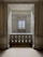 An elegant space with marble walls and a decorative balustrade. A window with a grid design is centered in the background, allowing soft light to enter the room, creating a calm and serene atmosphere.