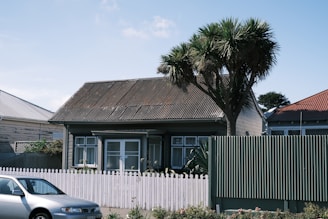 A cozy single-family house with a small garden and white picket fence under blue sky.