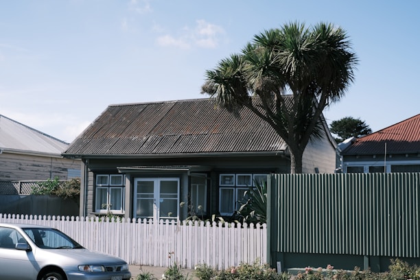 A cozy single-family house with a small garden and white picket fence under blue sky.