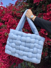 Woman holding a violet-toned accessory bag with delicate handmade details.