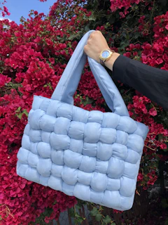 Hand holding a pastel lavender crochet bag with intricate patterns against a blurred garden backdrop