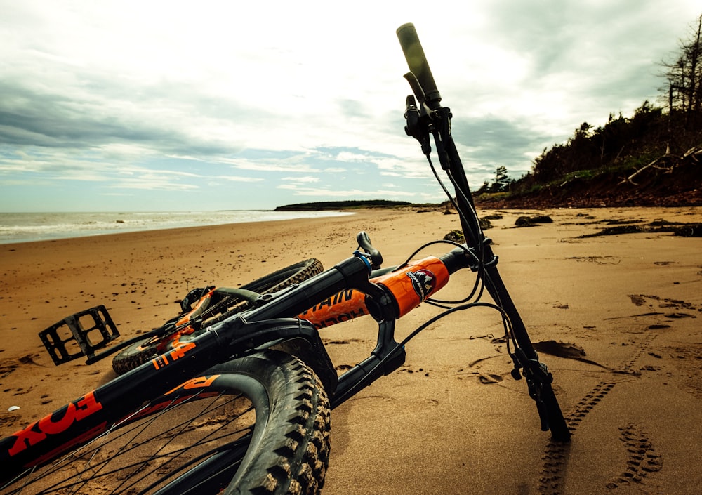 낮 동안 갈색 모래 위에 검은 색과 주황색 자전거