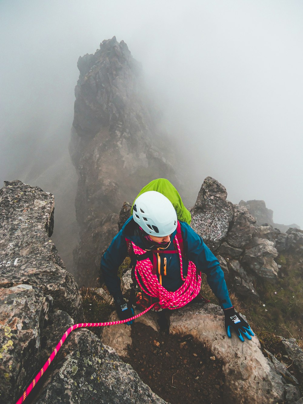 person in green and blue helmet and blue jacket standing on rock formation during daytime