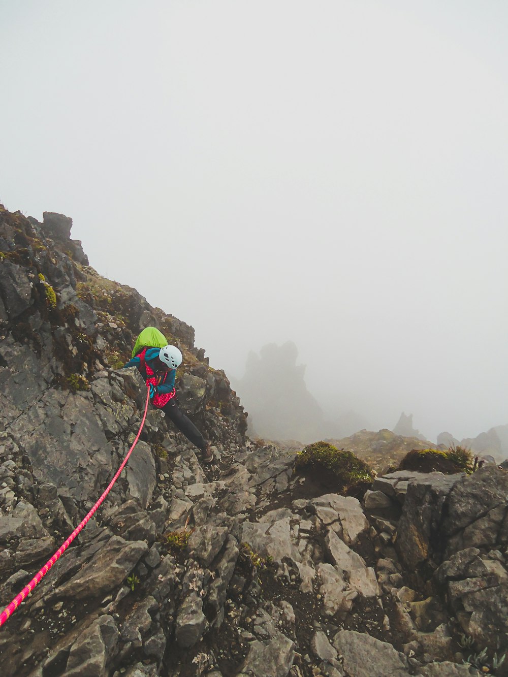 man in green jacket and blue pants with red and black hiking backpack standing on rocky