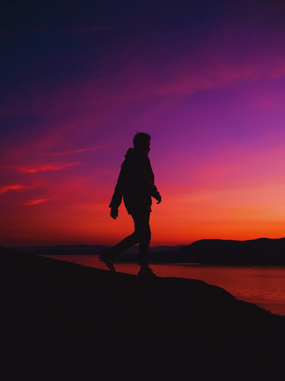 silhouette of woman standing on rock formation near body of water during sunset