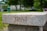 A stone bench with the word 'TRUST' engraved on its side is set in a lush, green park. The background features trees, blurred foliage, and a few indistinct people, creating a serene and calming atmosphere.