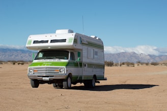 A vintage-style RV is parked on a vast sandy desert landscape, with distant mountains under a clear blue sky.