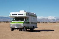 A vintage-style RV is parked on a vast sandy desert landscape, with distant mountains under a clear blue sky.
