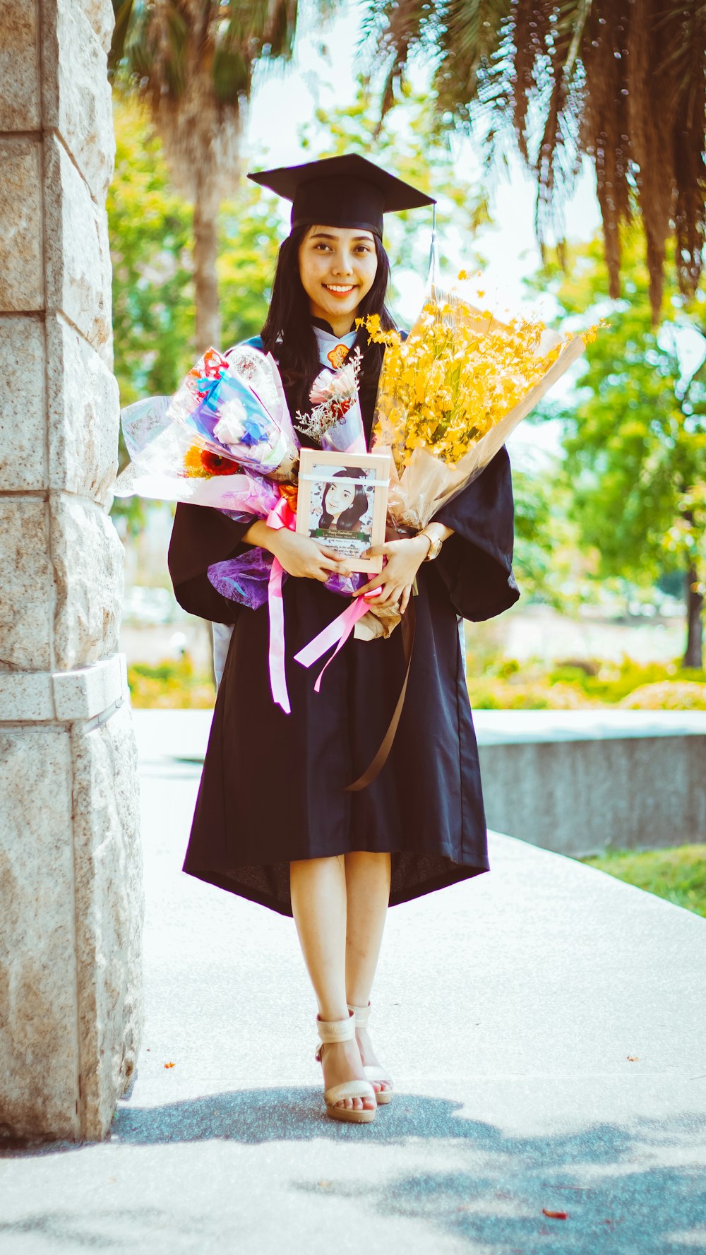 Femme en robe académique noire et violette tenant un bouquet de fleurs