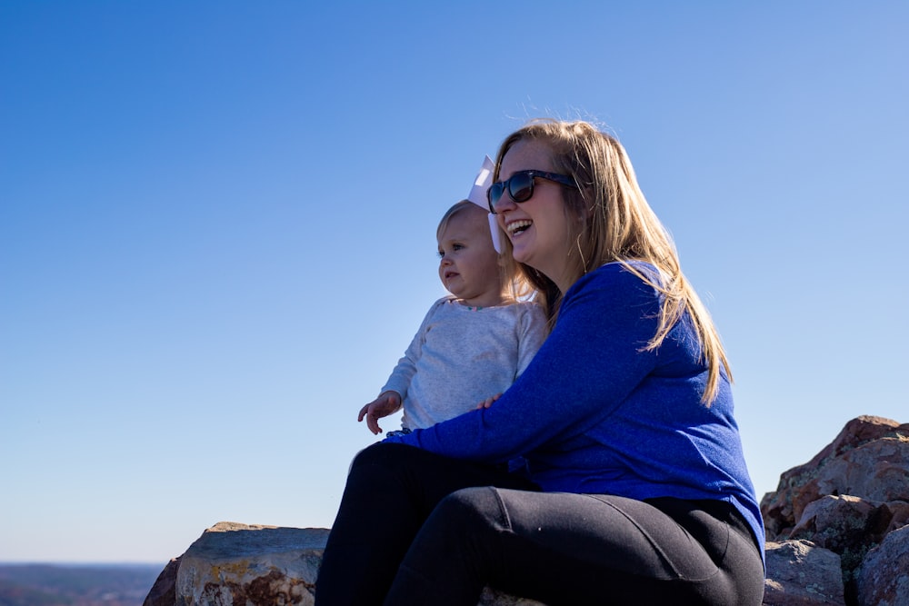 woman in blue sweater and black pants sitting on rock during daytime