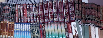A shelf filled with a variety of books, many of which have ornate and decorative covers. The books are organized in a neat, orderly manner, with the majority of the covers featuring intricate patterns and Arabic script.