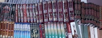 A shelf filled with a variety of books, many of which have ornate and decorative covers. The books are organized in a neat, orderly manner, with the majority of the covers featuring intricate patterns and Arabic script.