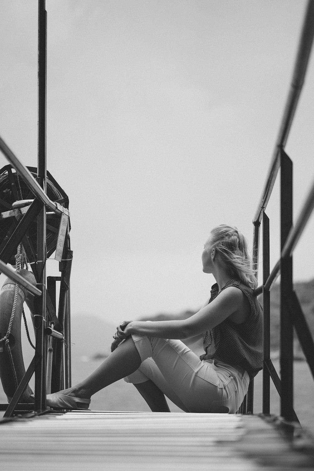 grayscale photo of woman in tank top sitting on ladder