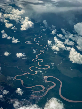 An aerial shot of a winding river cutting through lush green landscapes, seen from a paramotor's perspective.