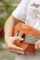 person in white t-shirt playing brown acoustic guitar
