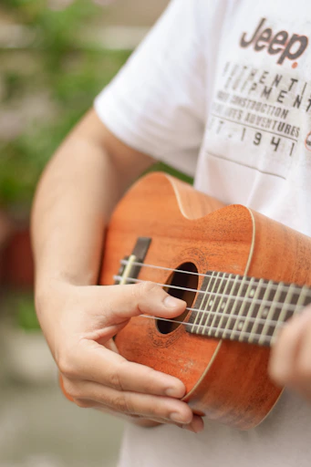 person in white t-shirt playing brown acoustic guitar